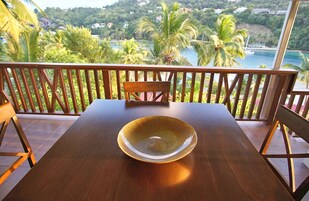 Una mesa de madera con un cuenco de vidrio, una silla y un balcón con vistas a un paisaje costero.