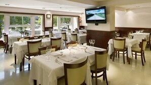 A restaurant with multiple tables set for dining, a television mounted on the wall, and large windows allowing natural light. - Bristol (Buenos Aires)
