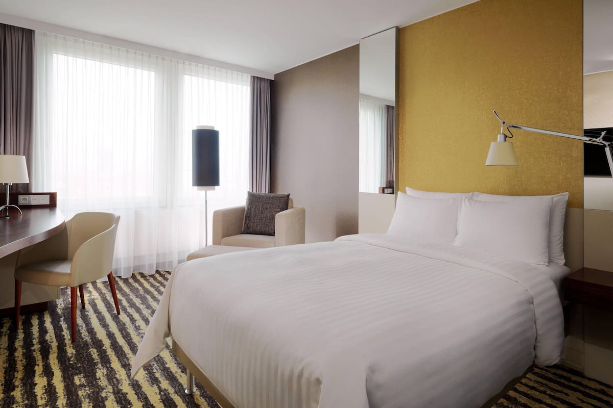 Hotellihuone, jossa on suuri sänky, työpöytä tuolilla, sohva ja suuri ikkuna, jossa on verhot.