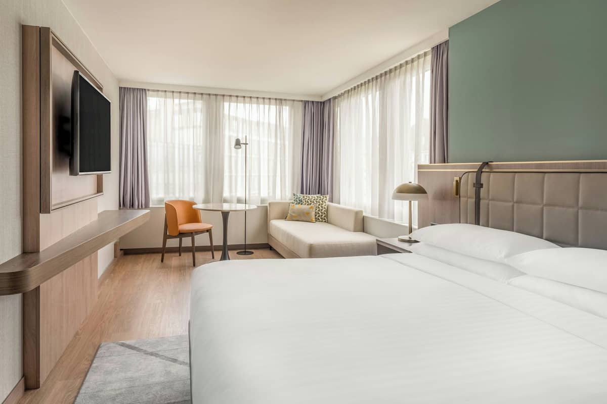 Hotellihuone, jossa on sänky, työpöytä, tuoli, televisio ja ikkuna, jossa on verhot.