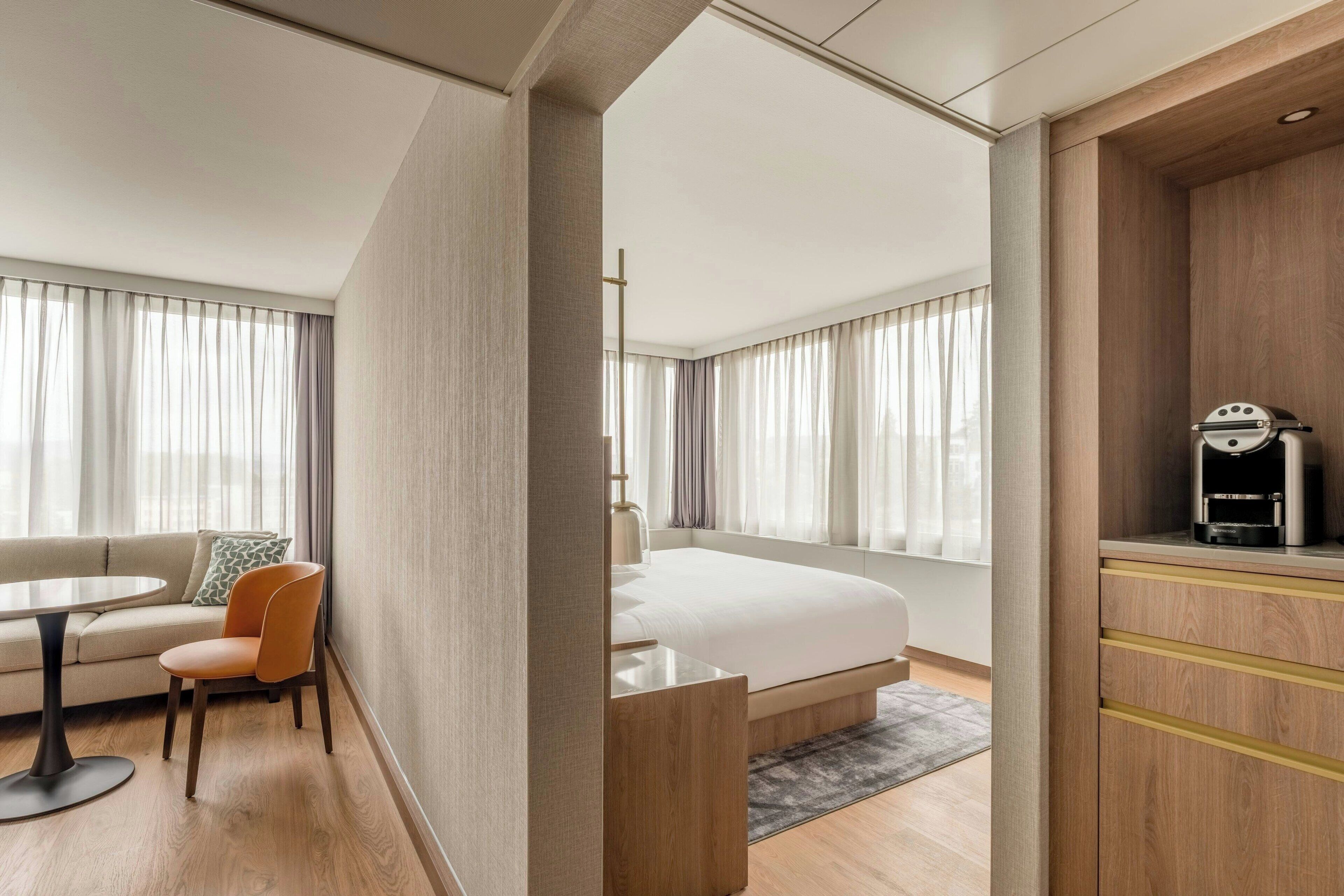 Ett modernt hotellrum med en säng, en soffa, ett matbord och en kaffemaskin.