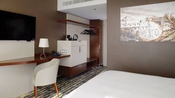 Quarto de hotel com cama, secretária com cadeira, televisão, máquina de café e quadro na parede.