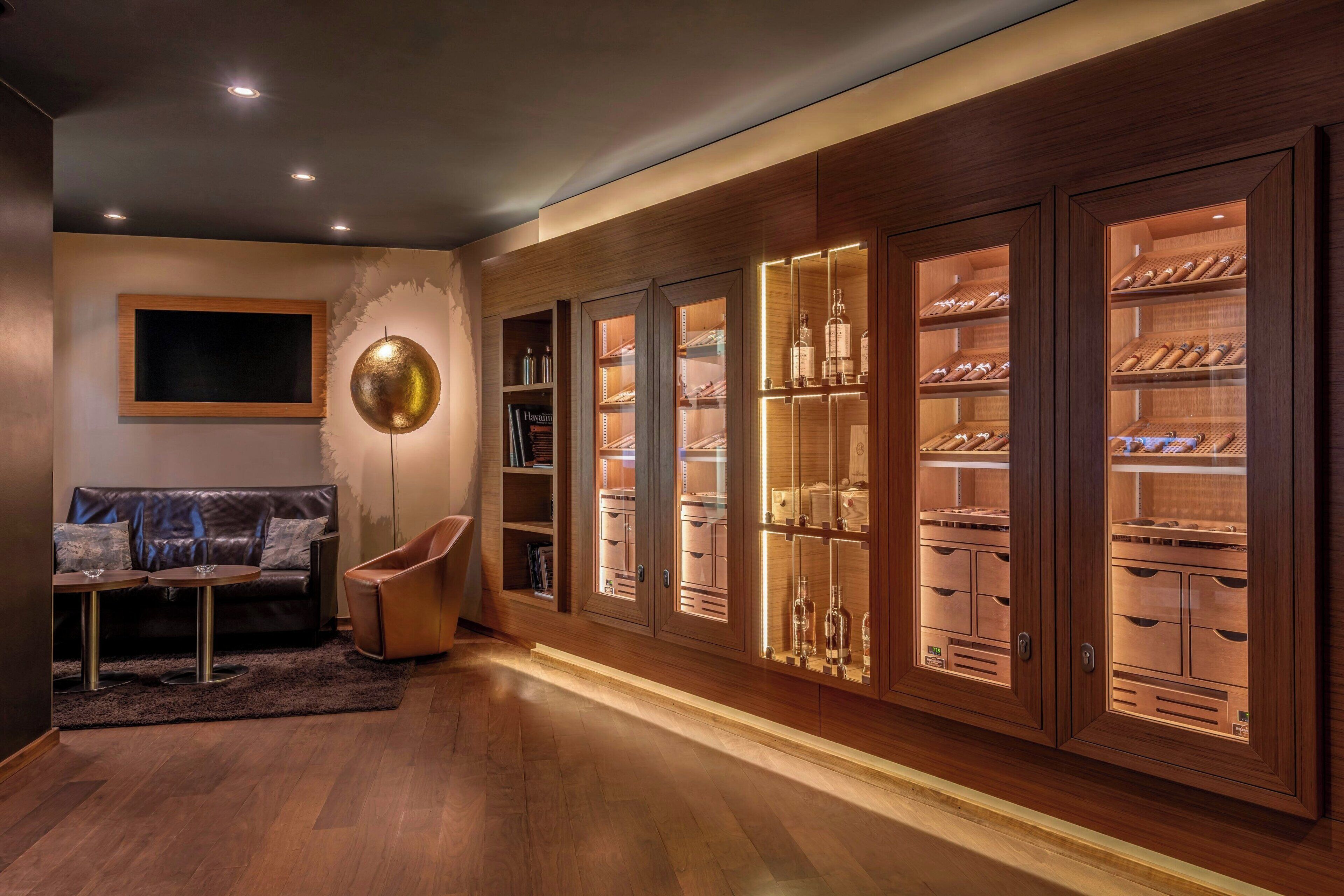 A modern living room with a wooden cabinet displaying shoes and bottles, a leather sofa, and a round table with a lamp.