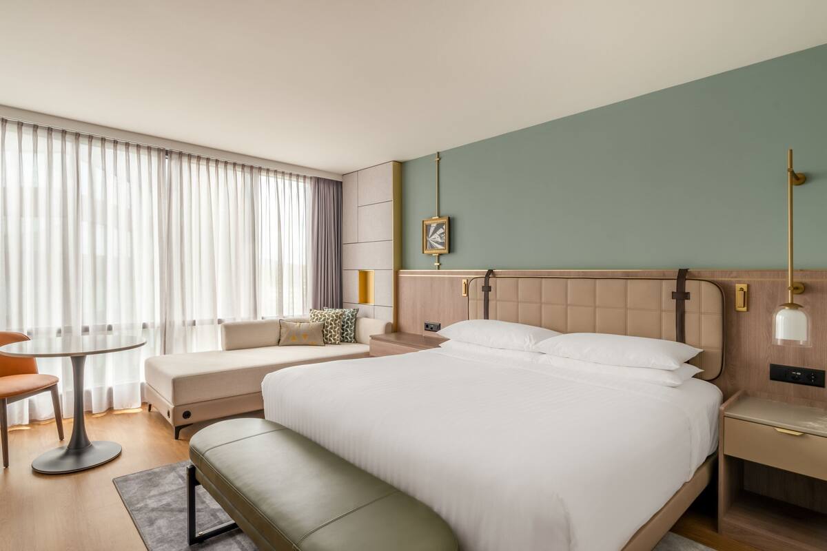 Moderni hotellihuone, jossa on suuri sänky, yöpöytä, työpöytä, tuoli ja ikkuna, jossa on verhot.