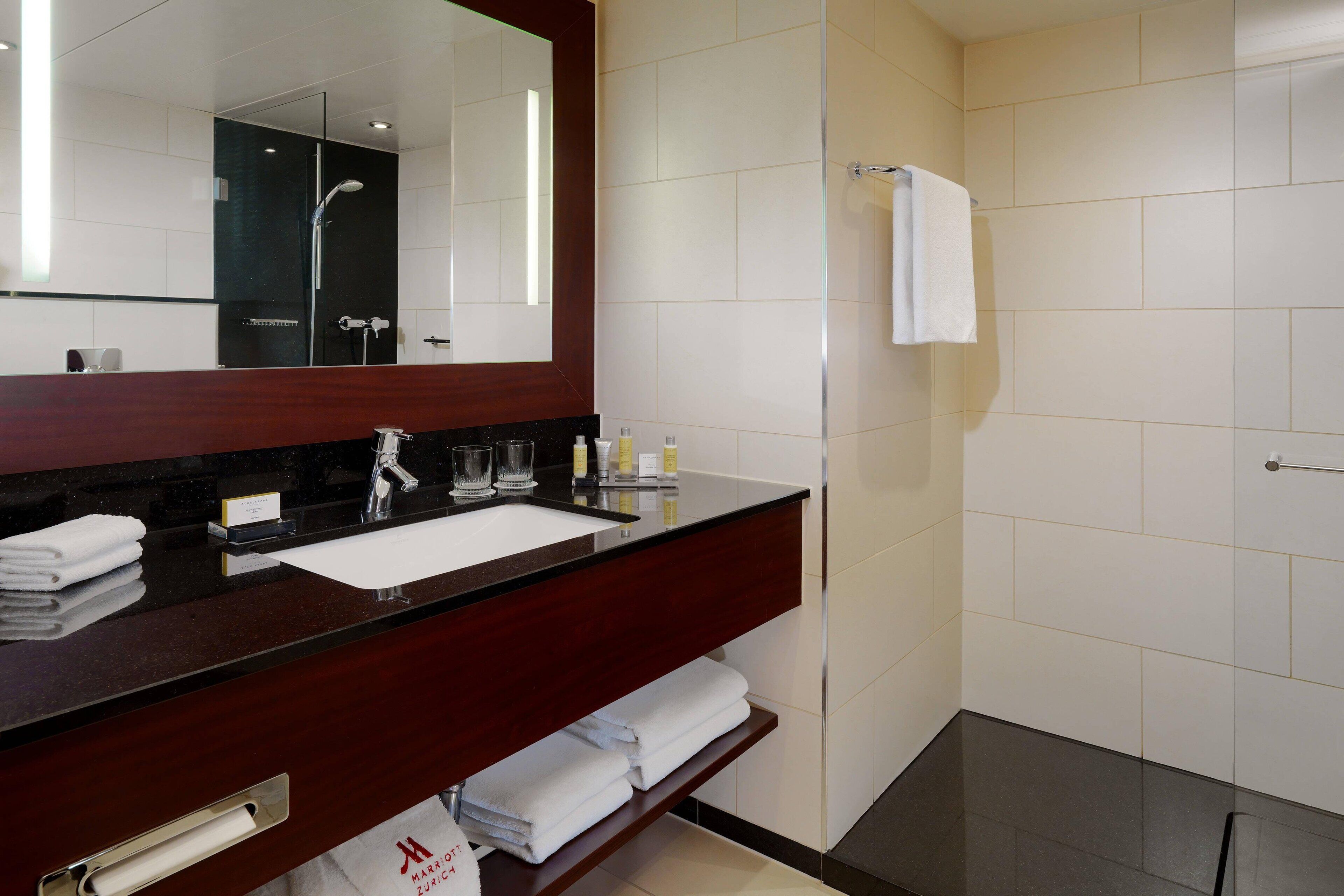 A modern bathroom with a dark wood vanity, a large mirror, a white sink, and a glass-enclosed shower.