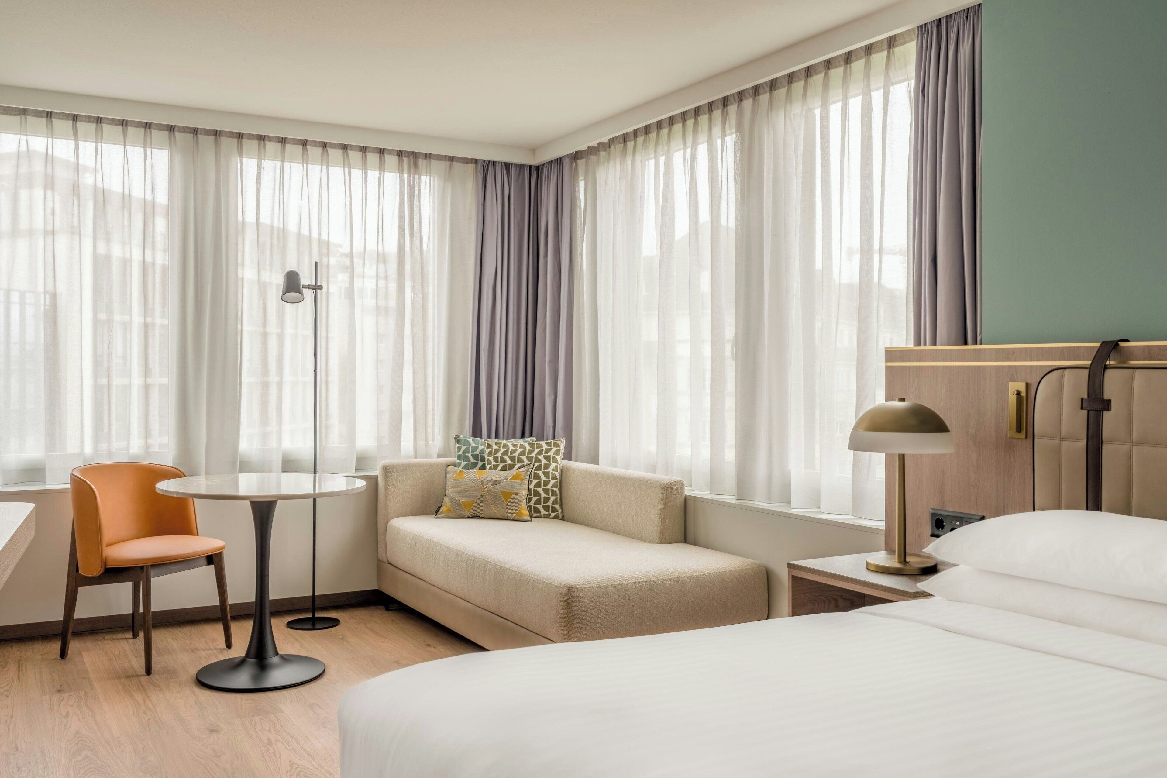 Una habitación de hotel con una cama, un sofá, una silla, una mesita y una lámpara.