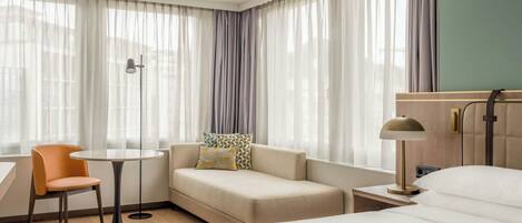 Una habitación de hotel con una cama, un sofá, una silla, una mesita y una lámpara.