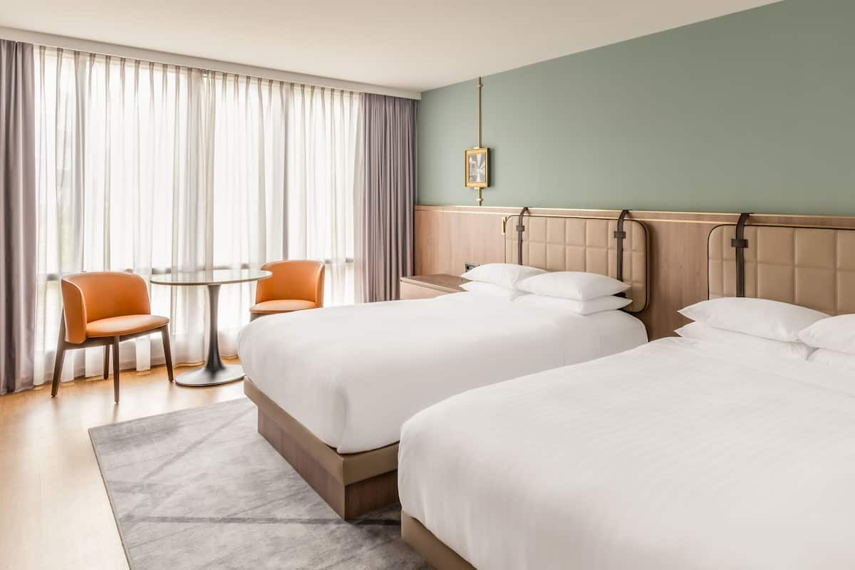 Hotellihuone, jossa on kaksi sänkyä, pyöreä pöytä ja kaksi tuolia.