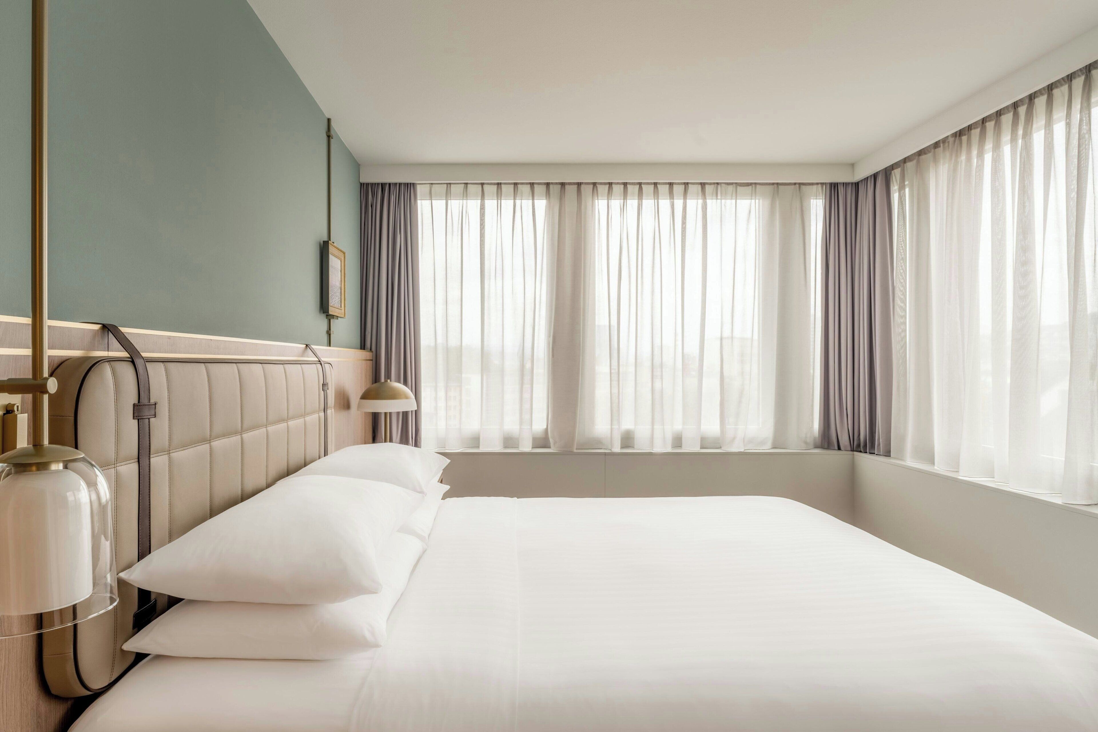 Ein Hotelzimmer mit einem großen Bett, einer Kopfteil und einem Fenster mit Vorhängen.