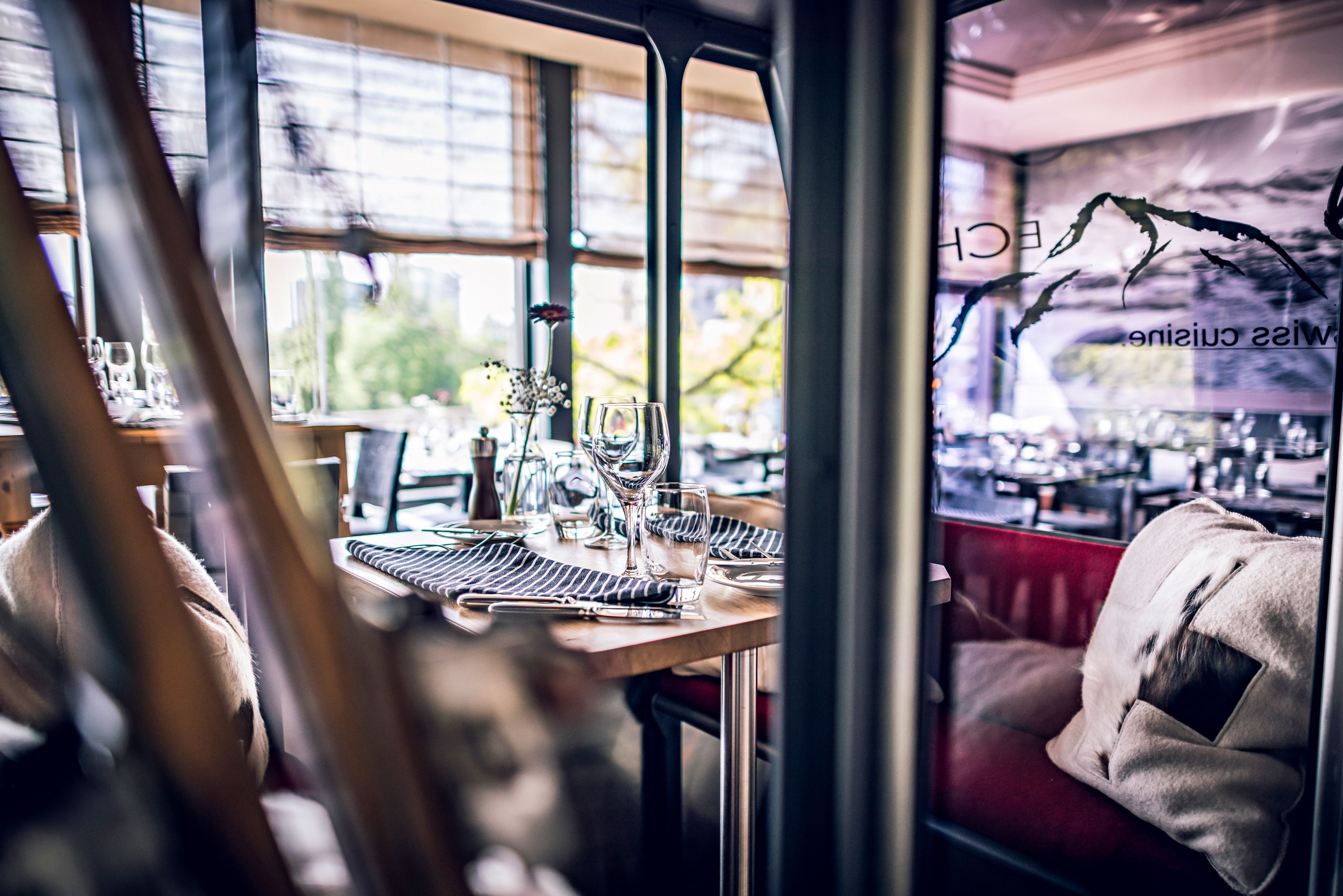 A restaurant interior with tables set for dining, large windows, and a view of the outdoors.