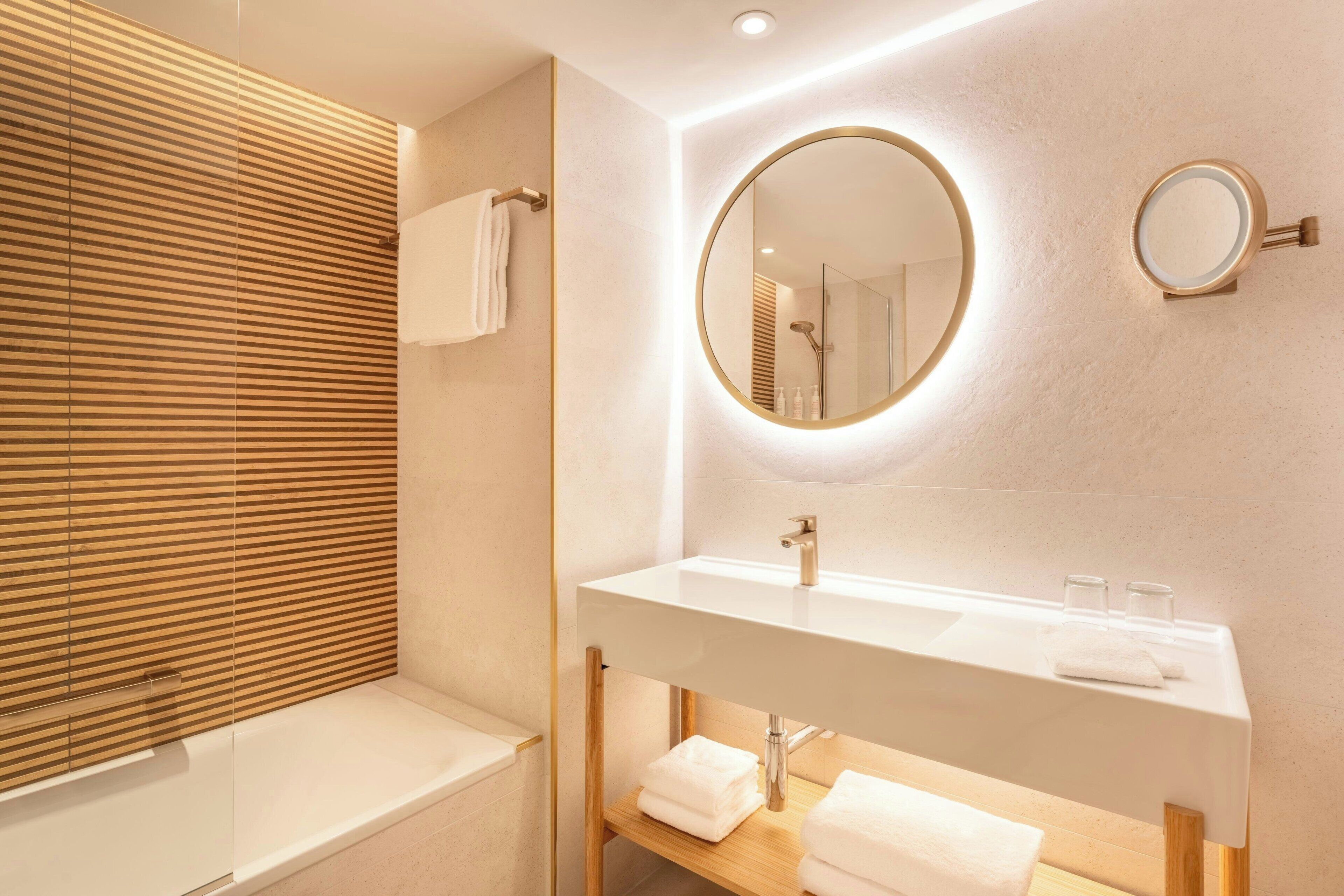 Un baño moderno con tocador de madera, un espejo redondo y una bañera.