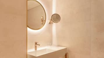 Une salle de bain avec un lavabo blanc, un robinet doré et un miroir rond doté d’un cadre doré.