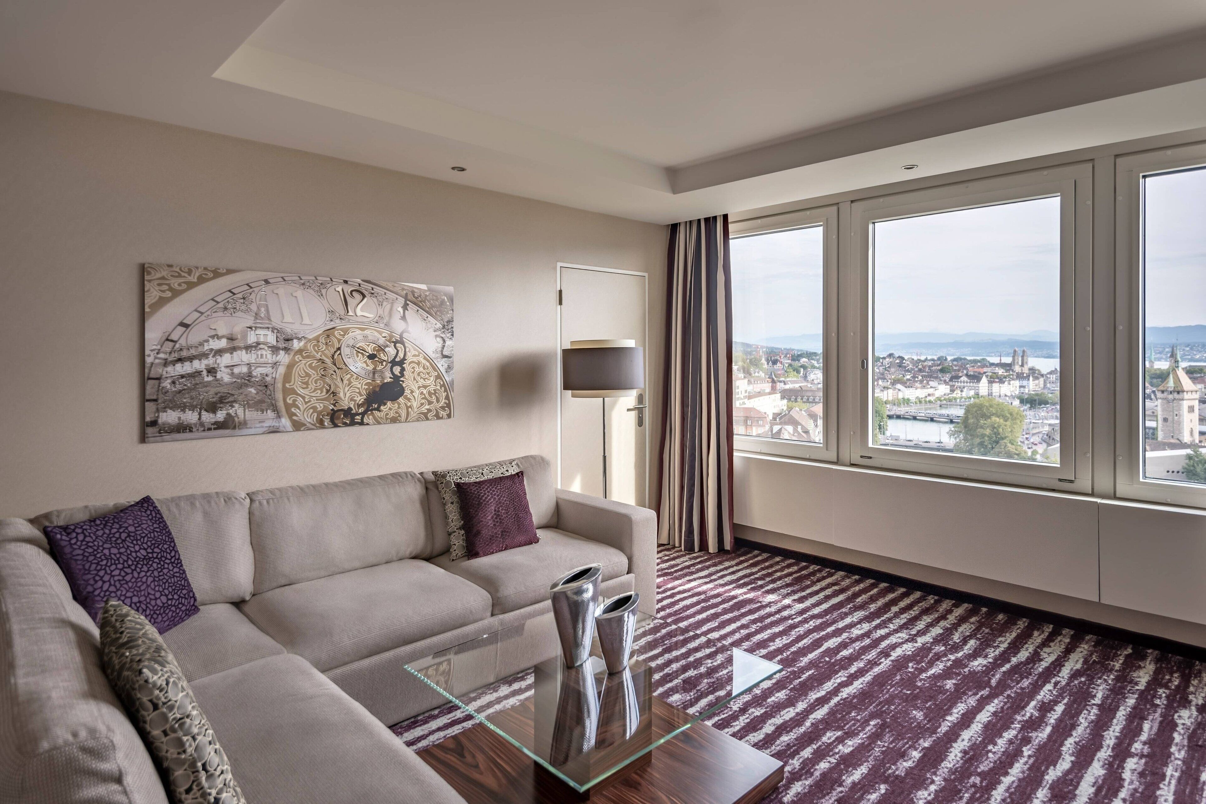 A modern living room with a large window, a sofa, a coffee table, and a city view.