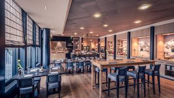 A modern restaurant with a bar area, wooden flooring, and large windows.