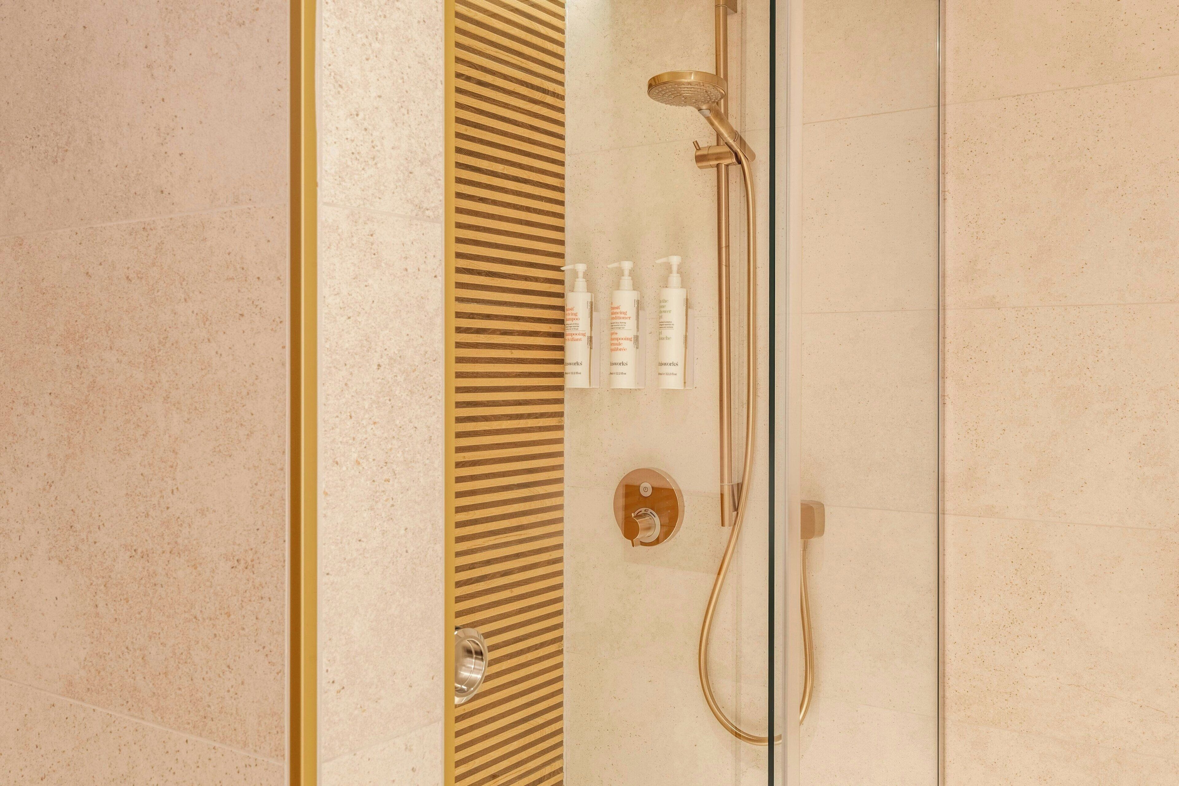 A modern bathroom with a glass-enclosed shower, gold accents, and toiletries on the wall.