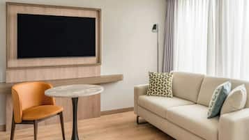 A modern living room with a flat-screen TV mounted on the wall, a round coffee table, a beige sofa with patterned cushions, and a wooden floor.