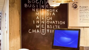 A wooden desk with a computer monitor, keyboard, and mouse. A chalkboard with words like "SOCIAL BUSINESS NETWORK MEDIA" is visible. - ibis Paris Gennevilliers (Gennevilliers)