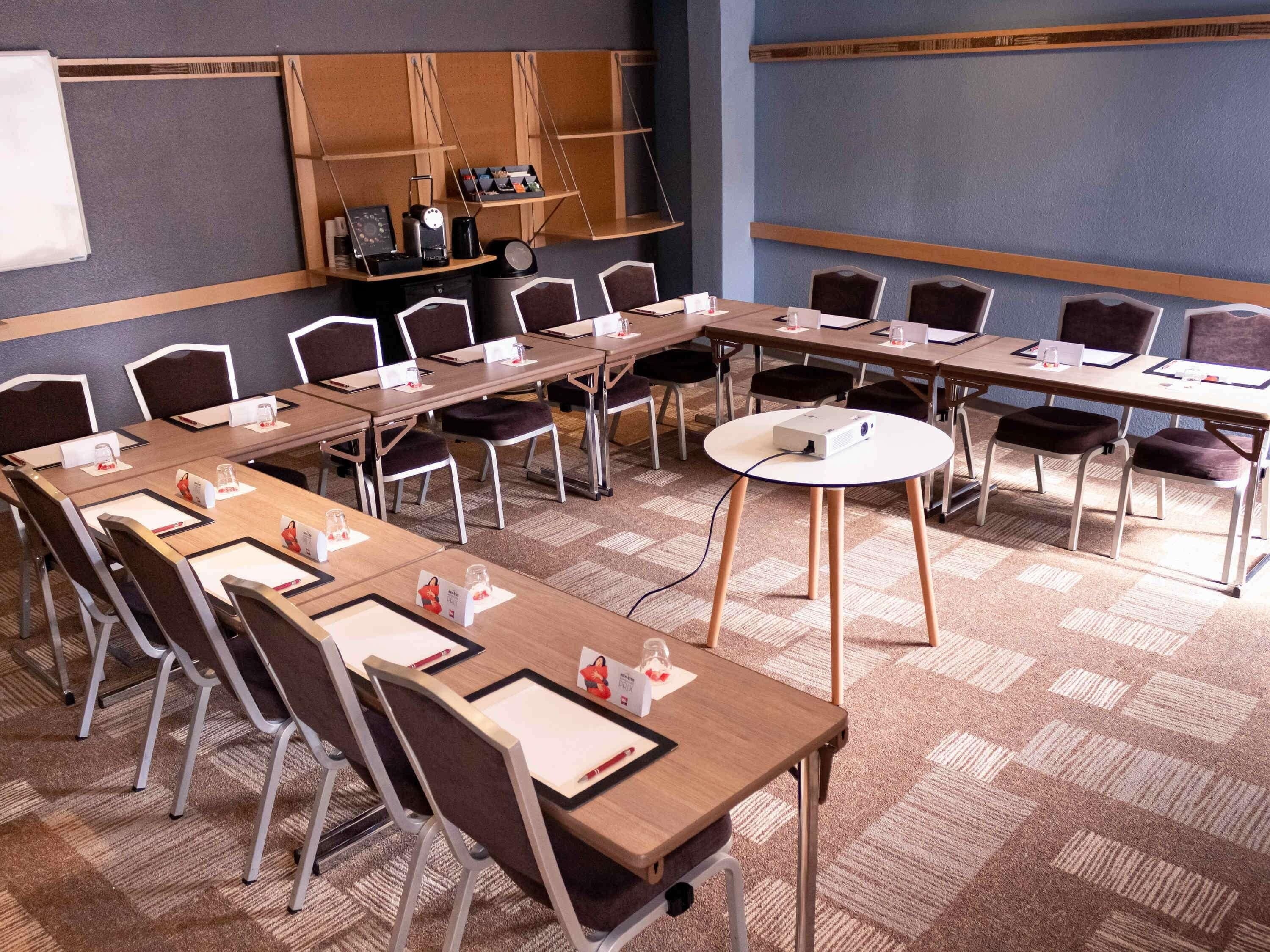 Een congrescentrum met lange tafels, stoelen, een beamer en een whiteboard.