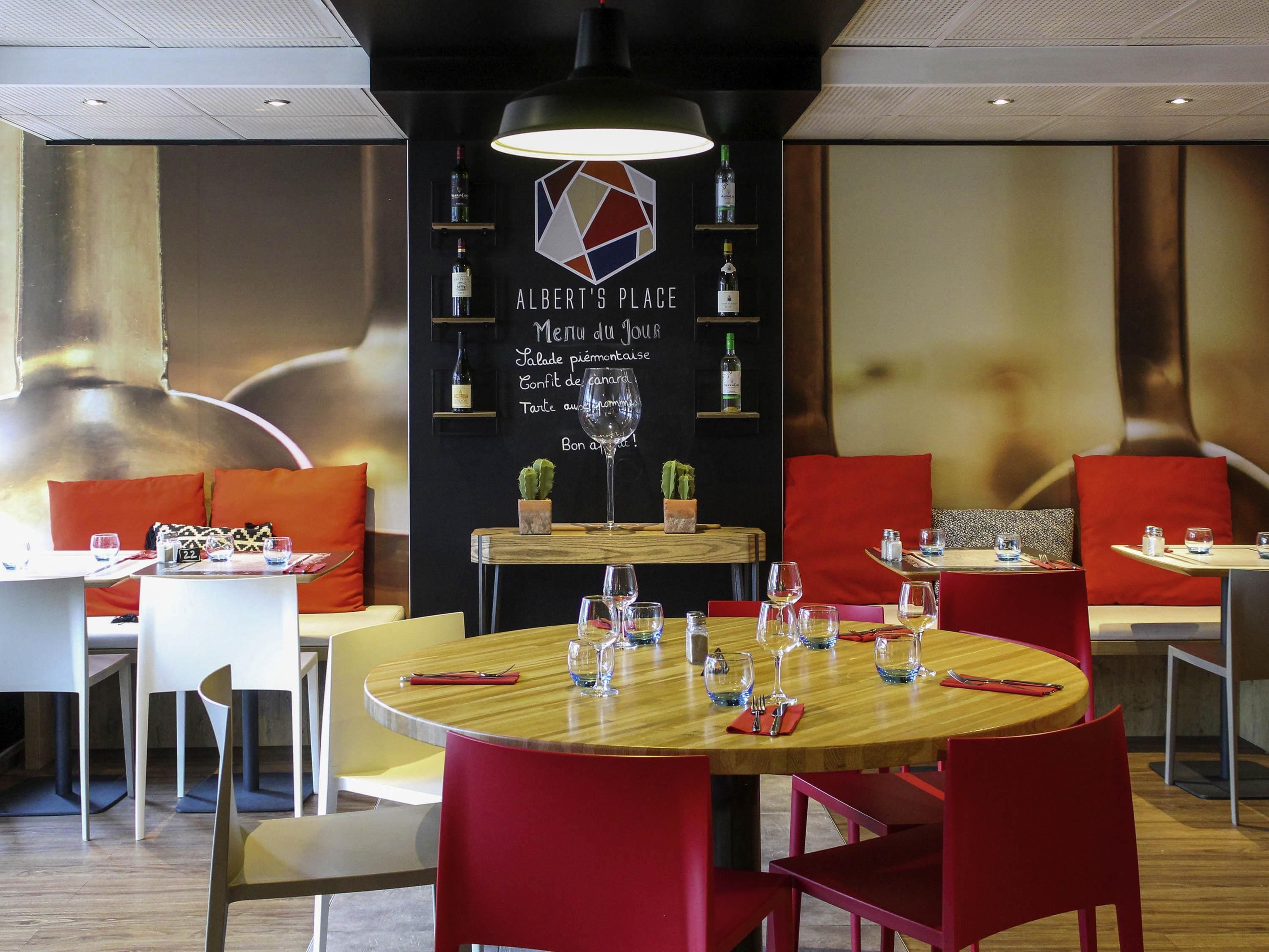 A restaurant interior with round tables, red chairs, and a black wall with menu options.