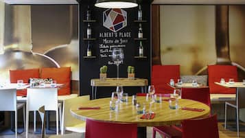 A restaurant interior with round tables, red chairs, and a black wall with menu options.