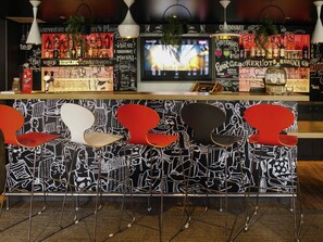 Eine Bar mit einer Wand in Schwarz-Weiß-Muster, einem Fernsehbildschirm und roten Stühlen.