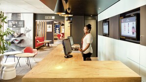 A modern hotel lobby with a wooden reception desk, comfortable seating areas, and digital displays on the walls. - ibis Paris Gennevilliers (Gennevilliers)