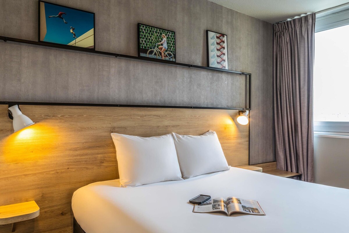 A hotel room with a large bed, a wooden headboard, and artwork on the wall.