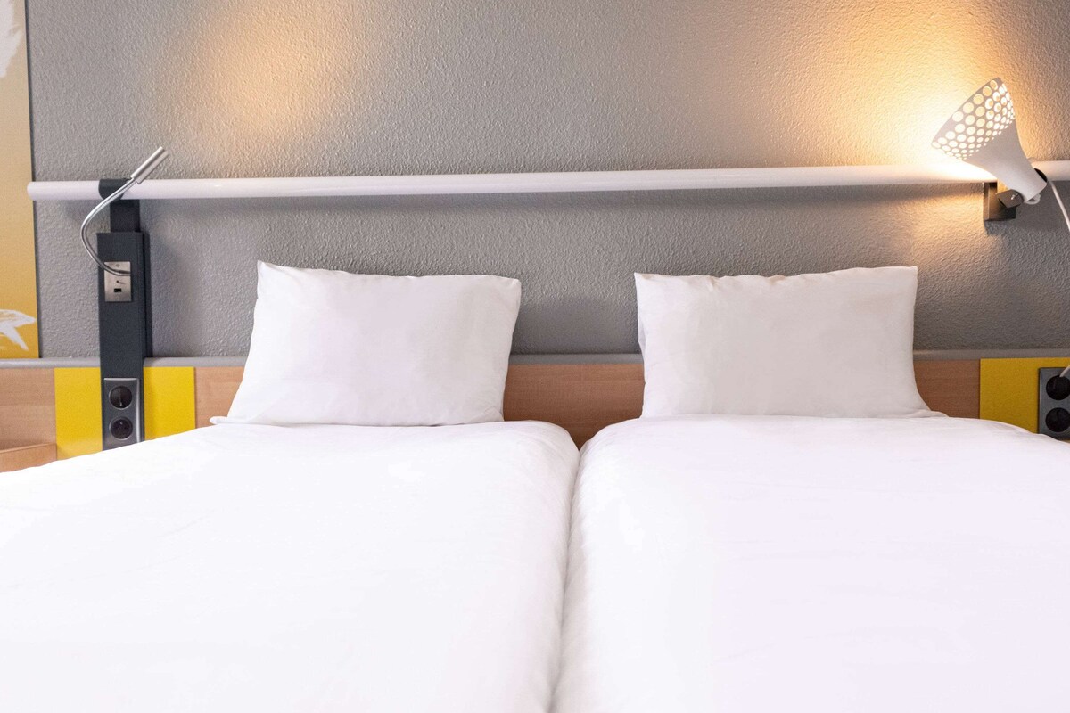 A hotel room with two single beds, a wall-mounted light, and a power outlet.