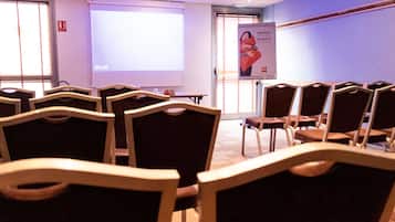 Une salle de conférence avec des rangées de chaises, un écran de projection et une banderole de bienvenue.