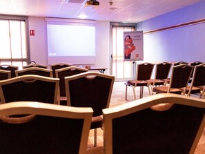 A conference room with rows of chairs, a projector screen, and a welcome banner.