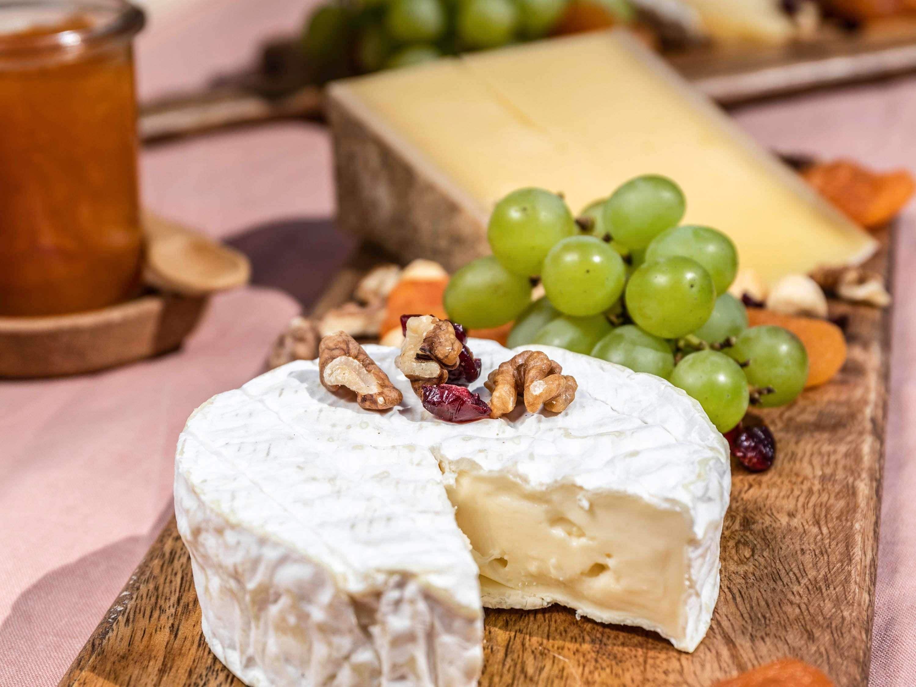 A wooden board with a wheel of cheese, green grapes, and nuts.