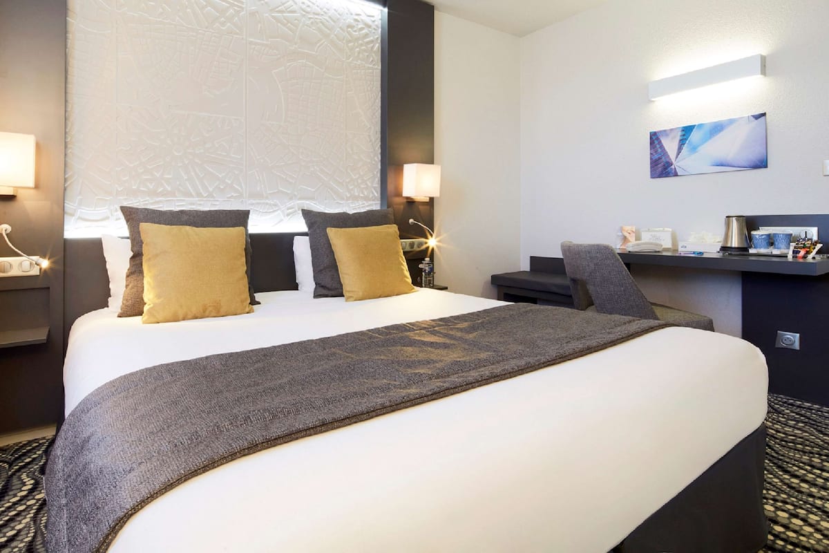 Een hotelkamer met een groot bed, een bureau met stoel en een wandtelevisie.