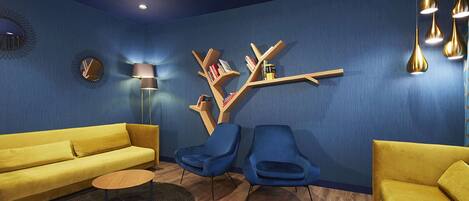 Una sala de estar moderna con pared azul, sofá amarillo, sillones azules y una estantería de madera.