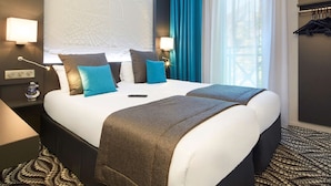 A hotel room with a large bed, two bedside tables, a wall-mounted TV, and a window with curtains. - Hôtel Kyriad Paris Bezons - La Défense (Bezons)