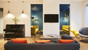 A modern living room with a piano, sofas, and a TV. - Hôtel Kyriad Paris Bezons - La Défense (Bezons)