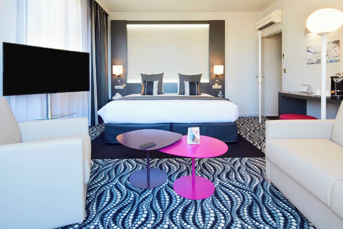Een hotelkamer met een groot bed, een flatscreen televisie, een koffiezetapparaat en een klein tafeltje met een stoel.