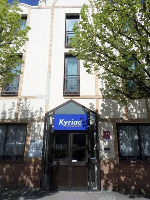 L’entrée d’un hôtel, avec une enseigne indiquant « Kyriad Hotel Restaurant ».