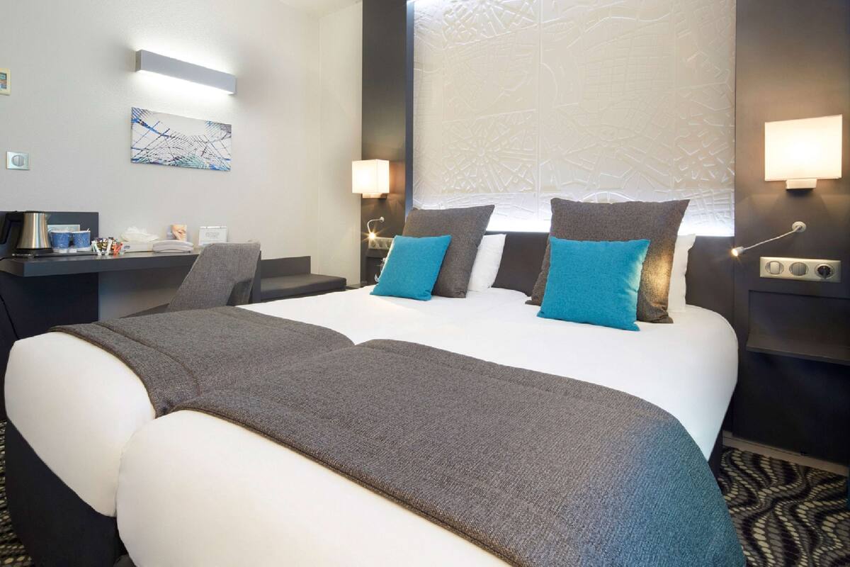 Een hotelkamer met een groot bed, twee nachtkastjes, een bureau met een computer en een aan de muur bevestigde televisie.