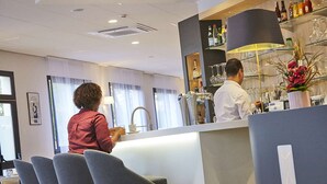 A bar area with a counter, bar stools, and a variety of bottles and glasses on shelves. - Hôtel Kyriad Paris Bezons - La Défense (Bezons)