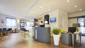 A modern hotel lobby with a reception desk, seating area, and a TV screen. - Hôtel Kyriad Paris Bezons - La Défense (Bezons)