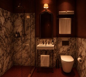 A bathroom with a marble wall, a sink, a toilet, a shower, and a towel rack. - Huxley House Hotel (Amsterdam)