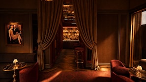 A dimly lit hallway with a bar area, red upholstered chairs, and a painting on the wall. - Huxley House Hotel (Amsterdam)