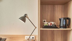 A desk with a desk lamp, a book, a kettle, and a cup on a wooden shelf. - Huxley House Hotel (Amsterdam)