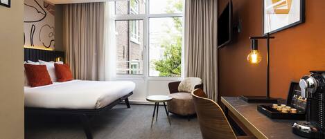 A hotel room with a bed, a chair, a desk with a coffee machine, a TV, and large windows with curtains.