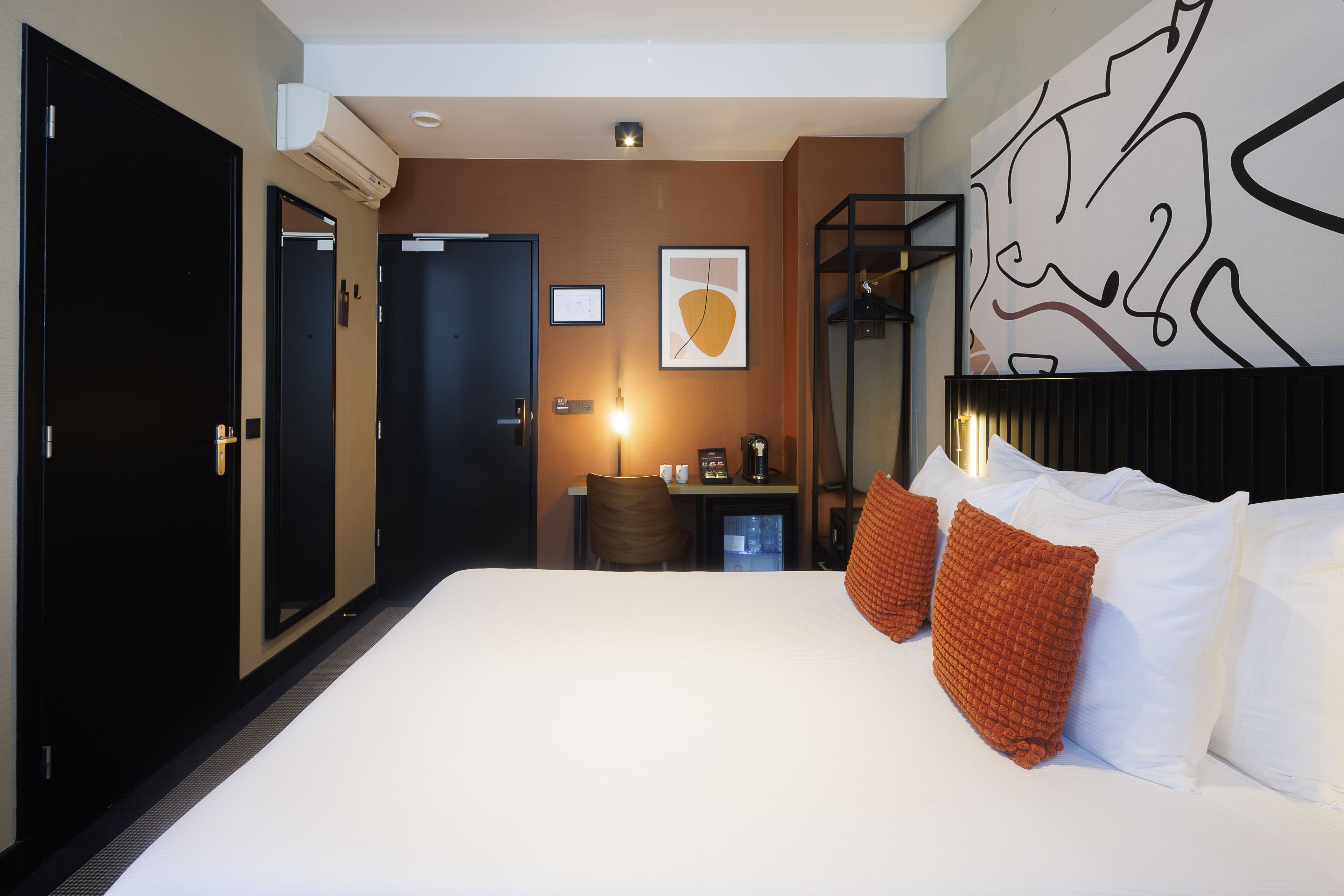 A hotel room with a large bed, a desk with a chair, a wall-mounted TV, and a framed picture.
