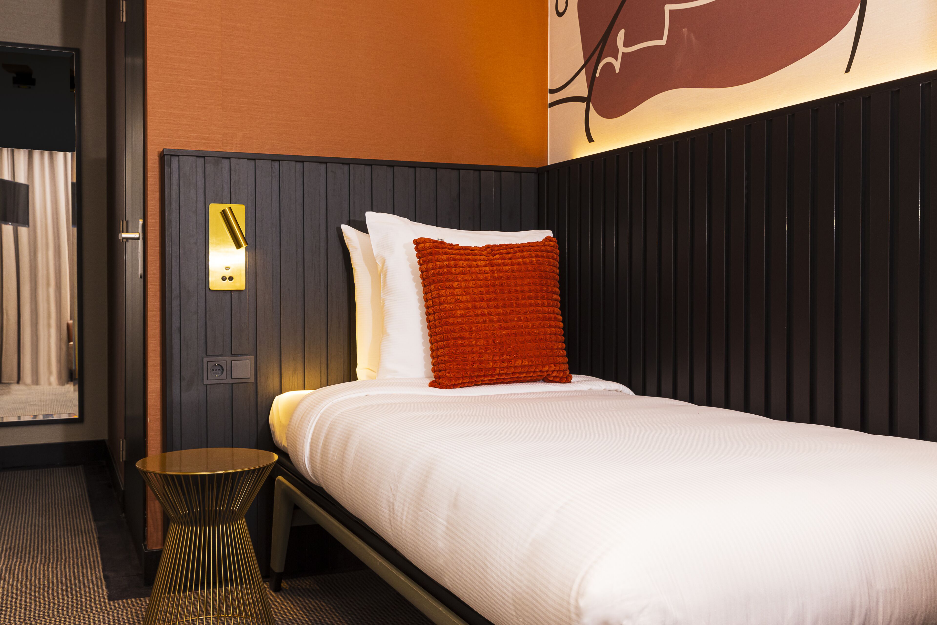 Una habitación de hotel con una cama, una mesita de noche, una lámpara de pared y un enchufe.
