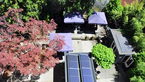 Eine Dachterrasse mit Solaranlagen, Sitzgelegenheiten im Freien mit Sonnenschirmen und umliegenden Bäumen.
