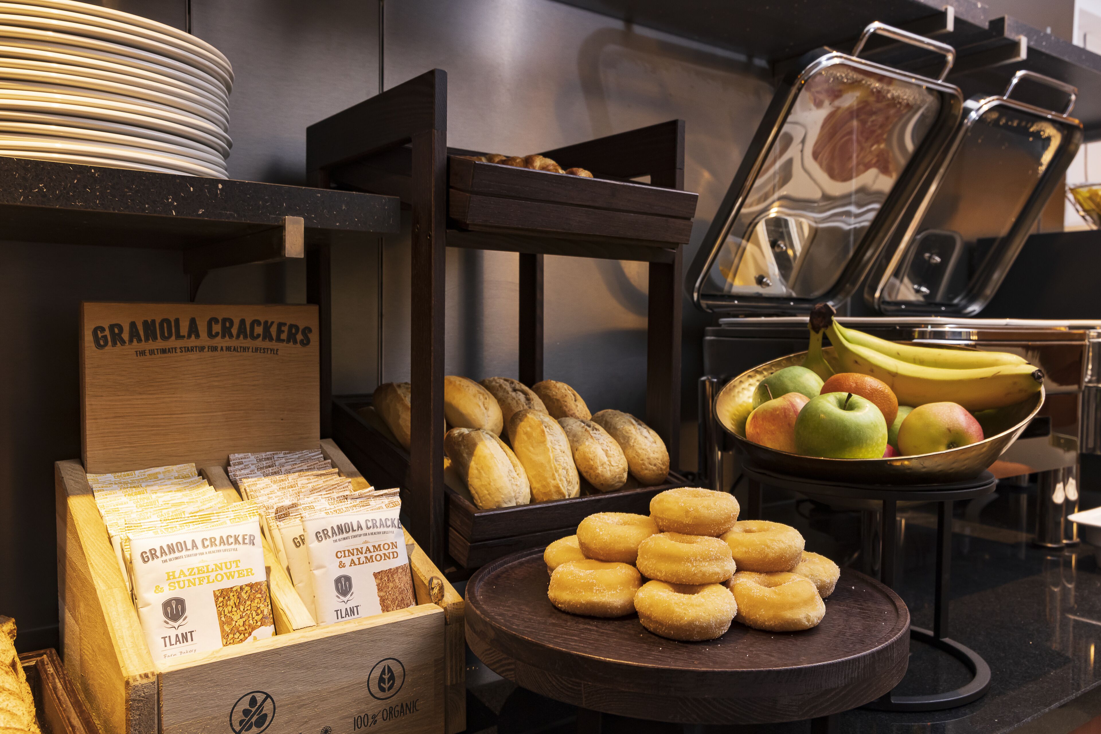 A buffet with granola crackers, bread, and a bowl of fruit.
