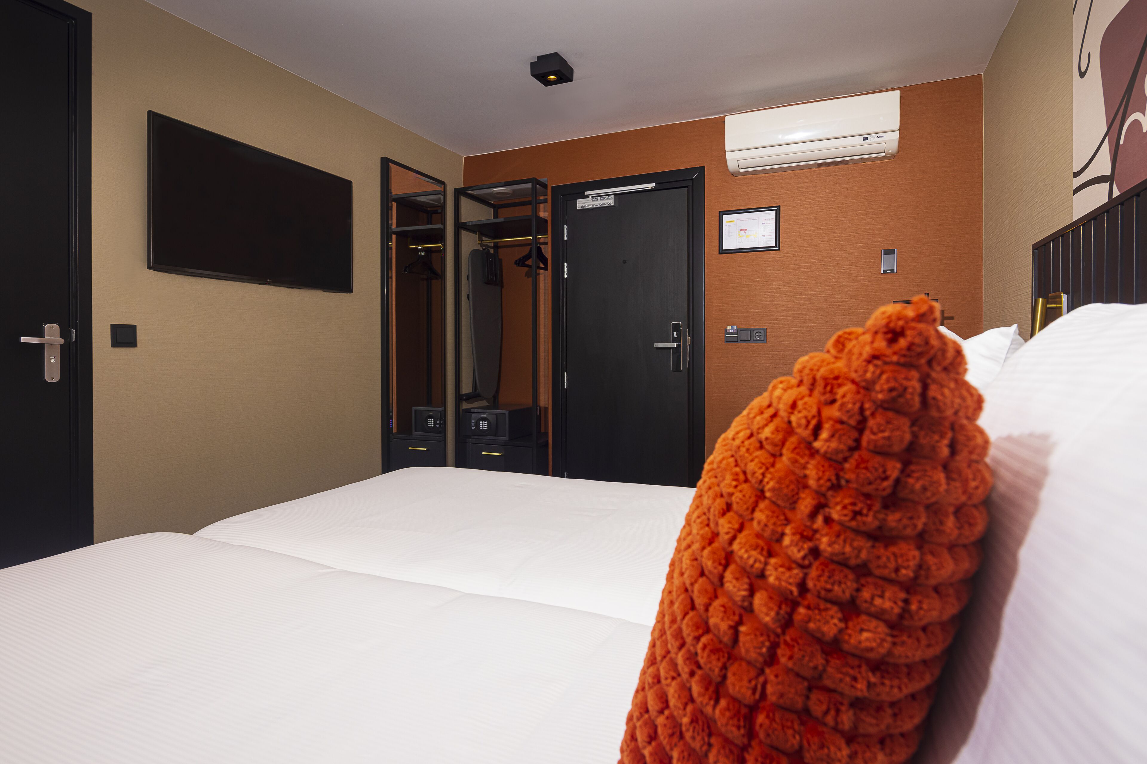 Une chambre d’hôtel avec un lit, une armoire, un miroir et un téléviseur fixé au mur.