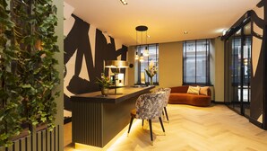 Ein modernes Wohnzimmer mit Holzdielen im Fischgrätmuster, einer schwarz-weißen abstrakten Wand, einer Bar mit Lampe und einer Couch mit Kissen.
